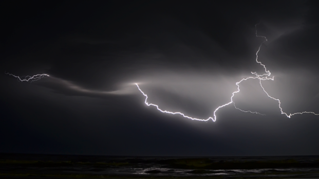 A bolt of white lightning flashes against the background of a dark sky. 